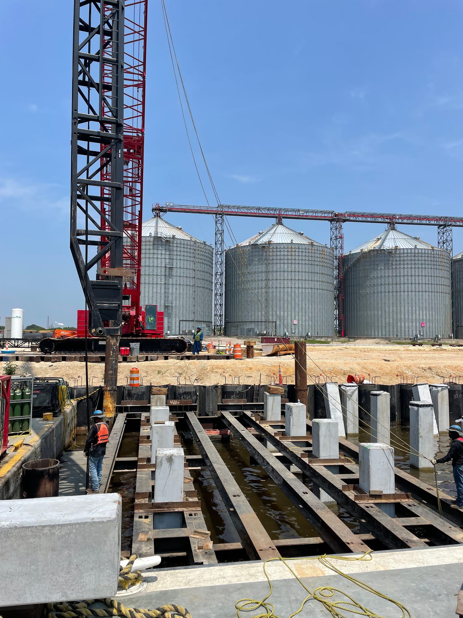 Construction management on an active jobsite: crane setting precast concrete elements near grain silos